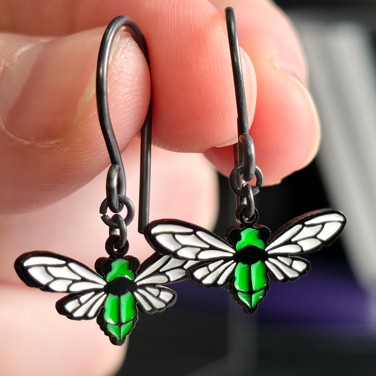 cicada dangle earrings held in fingers